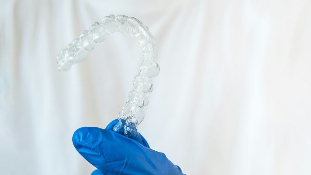 Adult man with gloves holds invisalign transparent braces for dental correction